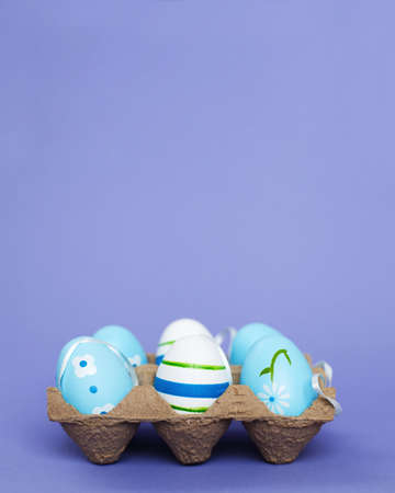 easter colorful handmade painted blue eggs in a box on purple background