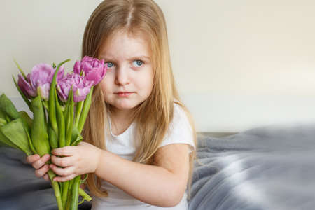 portrait of a happy smiling little girl with bouquet of flowers tulips in her handsの写真素材