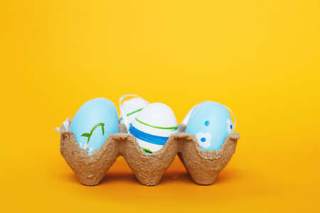 easter colorful handmade painted blue eggs in a box on orange background.
