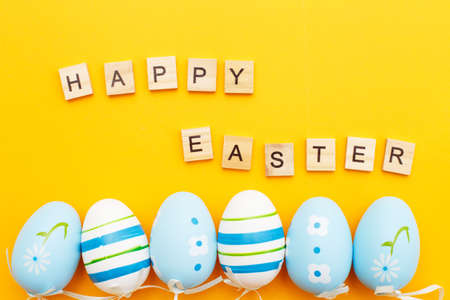 inscription happy easter with colorful handmade painted blue eggs on orange backgroundの写真素材