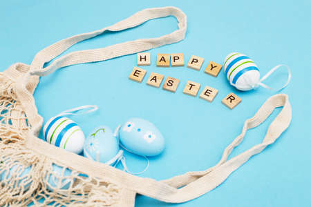 inscription happy easter with colorful painted eggs and cotton string bag on blue backgroundの写真素材