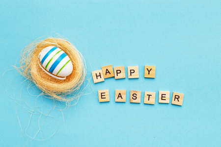 inscription happy easter with colorful handmade painted egg in the nest on blue backgroundの写真素材