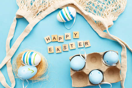 inscription happy easter with colorful painted eggs and cotton string bag on blue backgroundの写真素材