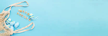 inscription happy easter with colorful painted eggs and cotton string bag on blue backgroundの写真素材