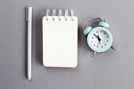 Top view of blank note paper with pen and alarm clock on gray backgroundの写真素材