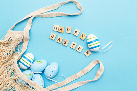inscription happy easter with colorful painted eggs and cotton string bag on blue backgroundの写真素材