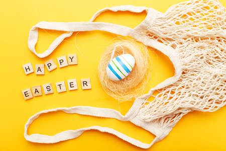 inscription happy easter with colorful painted eggs and cotton string bag on orange background