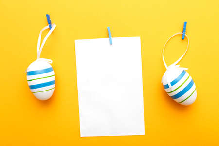 easter colorful eggs hanging on clothespins on orange background with sheet of paper for your textの写真素材