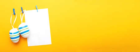 easter colorful eggs hanging on clothespins on orange background with sheet of paper for your textの写真素材