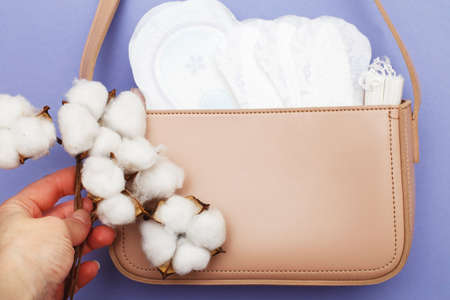 tampons, hygienic panty liners, feminine sanitary pads in a women's pink cosmetic bag on a purple background. hygiene and women's health care conceptの写真素材