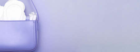 tampons, hygienic panty liners, feminine sanitary pads in a women's cosmetic bag on a purple background. hygiene and women's health care concept. bannerの写真素材