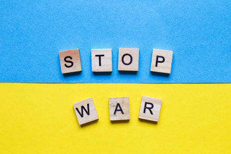 the inscription stop war made by wooden cubes on the ukrainian flag background.の写真素材