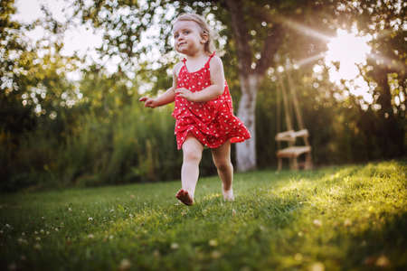 happy baby smiling. a little girl running in the garden at sunset outdoor barefootの写真素材