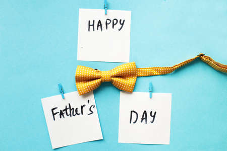 the inscription happy father's day on a white stickers hanging on clothespins with yellow bow tie on blue background.の写真素材