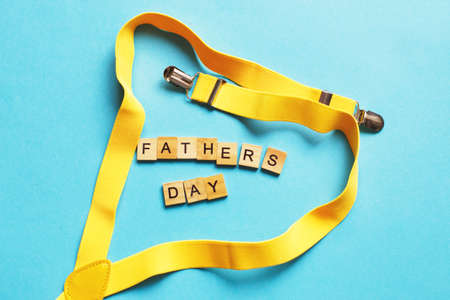 happy father's day lettering made by wooden cubes on a blue background with a yellow suspenders.の写真素材