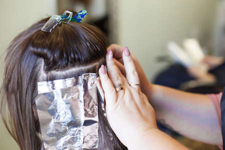 The hairdresser paints a brunette woman's hair in the beauty salon close