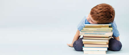 Upset schoolboy sitting with a pile of school books. boy sleeping on a stack of textbooks isolated...