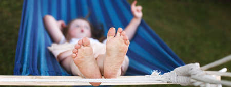 closeup of little girl's feet relaxing in the blue hammock during her summer vacation in the back yardの写真素材