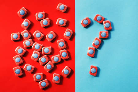 capsules for kitchen dishwashers and a question mark on a blue and red background. flat lay