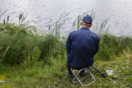 fisherman sitting back with a fishing rod on the shore of lake and catches fish.の写真素材