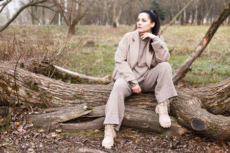 portrait of brunette woman in beige coat with beautiful long hair sitting on a tree in the park.の写真素材