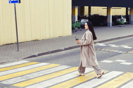woman holding coffee and crossing the road at pedestrian crossing against urban city background.の写真素材