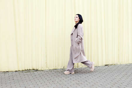 woman walking in a beige coat against urban city backgroundの写真素材