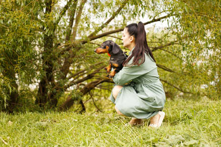 girl with her friend pet dog in the park. dachshund in the hands of his mistress.の写真素材