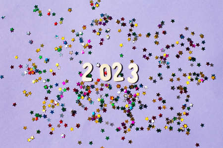 inscription 2023 with wooden numbers on a purple background with multicolored confetti in the form...
