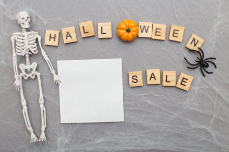 inscription halloween sale ,spider web and spiders on a gray background with skeleton and paper sticker with copy space