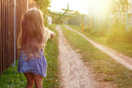 Happy child girl with long blond hair playing with toy airplane outdoor.の写真素材