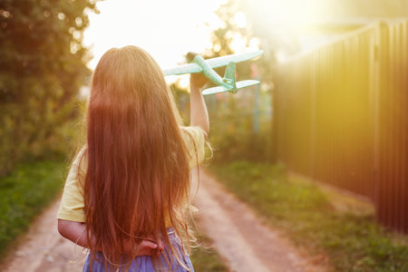 Happy child girl with long blond hair playing with toy airplane outdoor.の写真素材