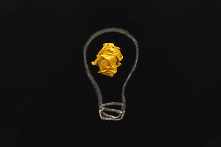 crumpled yelllow paper lightbulb as a concept creative idea and innovation on a blackboard background.の写真素材