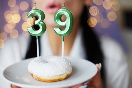 woman holding a cake with the number 39 candles on festive blurred bokeh background.の写真素材