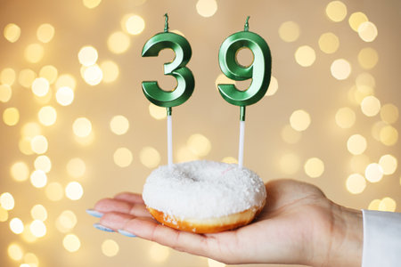 woman holding a cake with the number 39 candles on festive blurred bokeh background.の写真素材