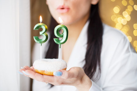 woman holding a cake with the number 39 candles on festive blurred bokeh background.