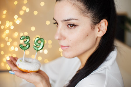 woman holding a cake with the number 39 candles on festive blurred bokeh background.の写真素材