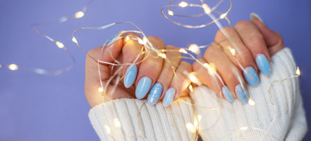 Cozy nails with winter manicure with snowflakes and lights on purple background.の写真素材