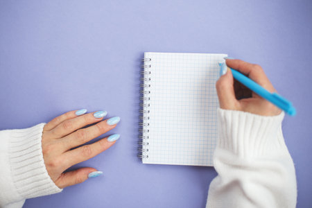 Woman hand with winter nails holding pen on notebook and writing wish list.の写真素材