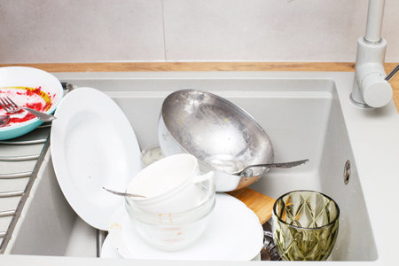 Pile of dirty dishes like plates, cutlery in the gray modern granite sink in the kitchen.の写真素材