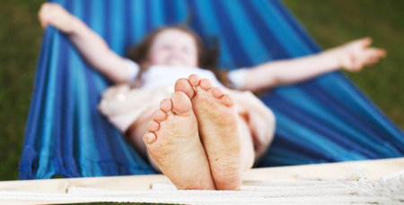 closeup of little girl's feet relaxing in the blue hammock during her summer vacation in the back yard. bannerの写真素材