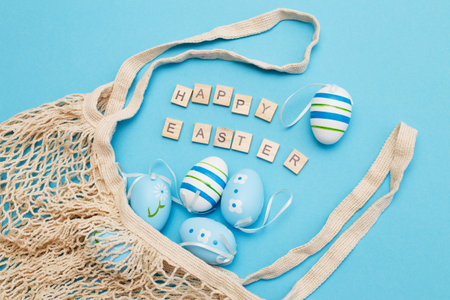 inscription happy easter with colorful handmade painted eggs and cotton string bag on blue background with copy space.の写真素材