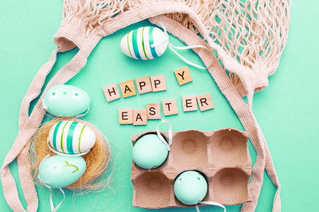 happy easter with colorful painted eggs and cotton string bag on green turquoise backgroundの写真素材