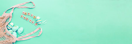 inscription happy easter with colorful painted eggs and cotton string bag on green background. bannerの写真素材