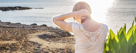 back view of a girl sitting on the sandy beach alone on the sea background. Bannerの写真素材