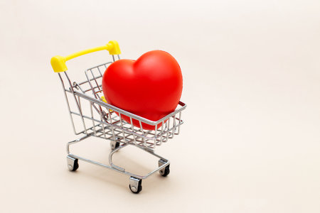 Red heart in the shopping cart or trolley isolated on beige background. Shopping for wedding, womens day concept, gifts for Valentines Day.の写真素材