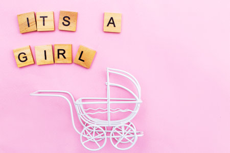 Its a girl. Little vintage white baby carriage stroller or pram on a pink background. Symbol of childbirth, parenthood, birth concept. Invitation festive greeting card on child birthday party.の写真素材