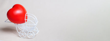 Red heart in the pram or carriage isolated on beige background. Symbol of childbirth. Valentine's Day or newborn greeting card. Bannerの写真素材