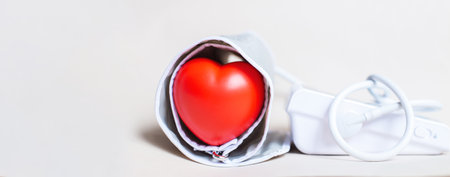 Red heart and white electronic tonometer isolated on beige background. Pressure measurement, health care and medicine, cardiology and hypertension problems concept. Bannerの写真素材