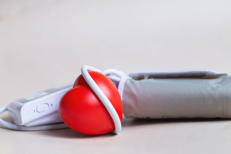 Red heart and white electronic tonometer isolated on beige background. Pressure measurement, health care and medicine, cardiology and hypertension problems concept.の写真素材